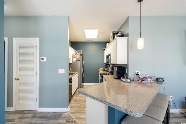 kitchen featuring a peninsula, light wood-type flooring, white cabinetry, dishwasher, and a breakfast bar