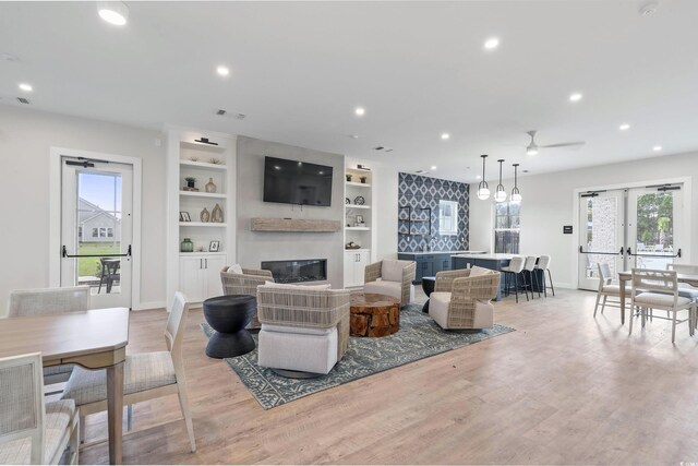 living room with a glass covered fireplace, plenty of natural light, baseboards, recessed lighting, and light wood finished floors