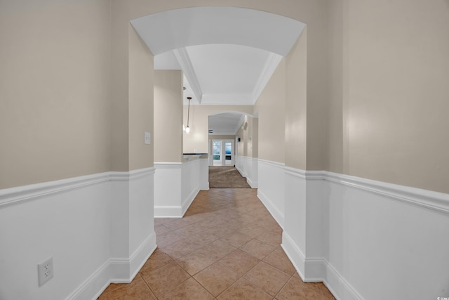 hallway with crown molding, wainscoting, light tile patterned floors, arched walkways, and baseboards