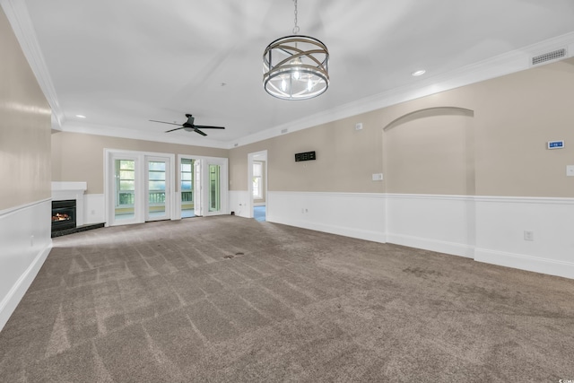 unfurnished living room with a wainscoted wall, carpet flooring, visible vents, ceiling fan with notable chandelier, and crown molding