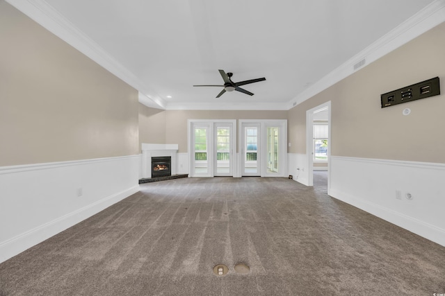 unfurnished living room featuring ceiling fan, a wainscoted wall, ornamental molding, carpet flooring, and visible vents