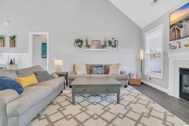 living area with visible vents, baseboards, a glass covered fireplace, and high vaulted ceiling