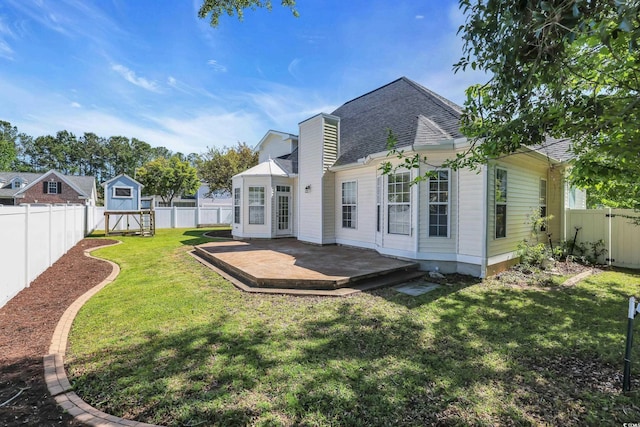 back of house featuring roof with shingles, a shed, a deck, a fenced backyard, and a lawn