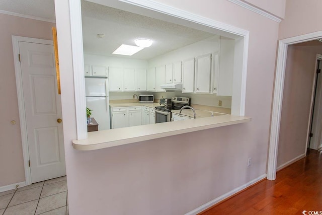 kitchen featuring white cabinets, under cabinet range hood, light countertops, baseboards, and appliances with stainless steel finishes