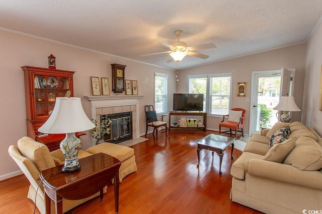 living room featuring wood finished floors, a ceiling fan, ornamental molding, a fireplace, and a textured ceiling