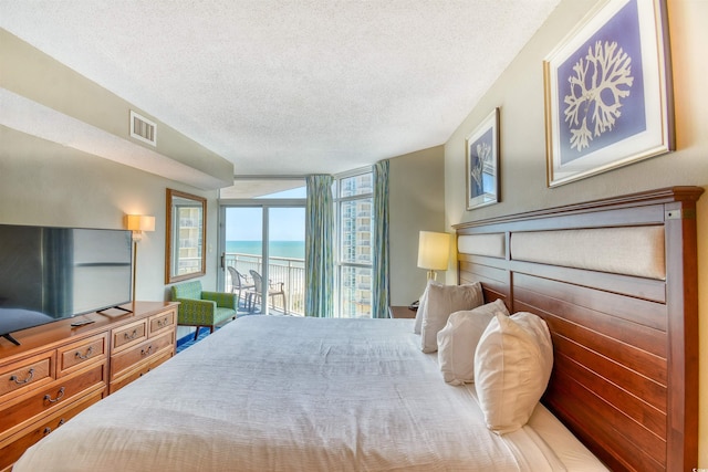bedroom with a water view, visible vents, a textured ceiling, and access to exterior
