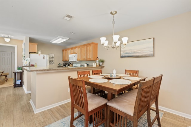 dining space featuring baseboards, a notable chandelier, light wood-type flooring, and visible vents