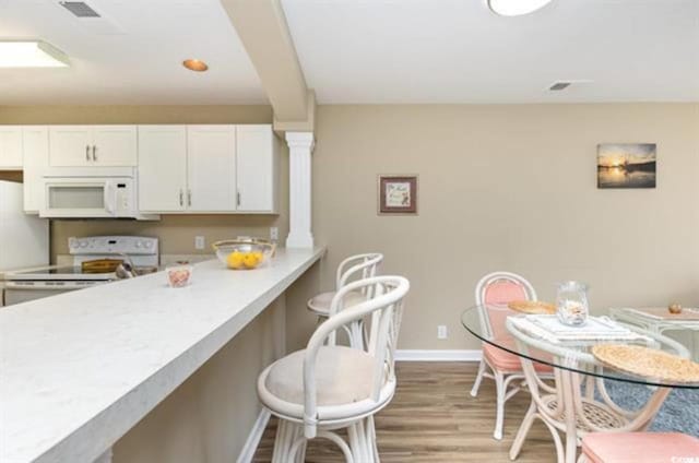 kitchen featuring white cabinets, a kitchen breakfast bar, wood finished floors, white appliances, and baseboards