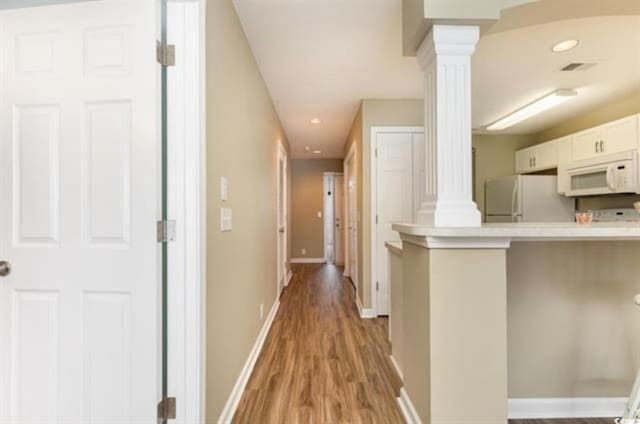 kitchen with light wood-type flooring, light countertops, decorative columns, and white appliances