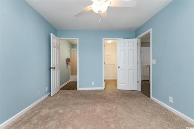unfurnished bedroom with carpet, a ceiling fan, a walk in closet, a closet, and baseboards