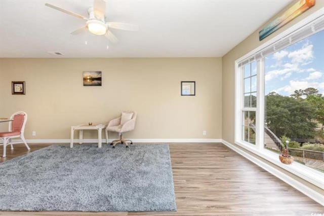 living area with baseboards, a ceiling fan, and wood finished floors