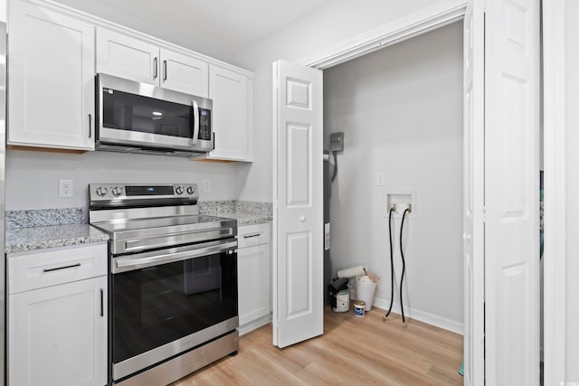 kitchen featuring light wood finished floors, white cabinets, light stone counters, and appliances with stainless steel finishes