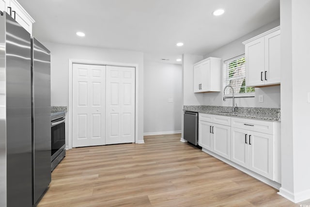 kitchen featuring light stone countertops, light wood-style flooring, baseboards, white cabinets, and appliances with stainless steel finishes