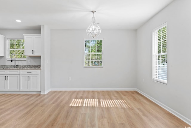unfurnished dining area featuring baseboards, light wood-style floors, an inviting chandelier, and a sink
