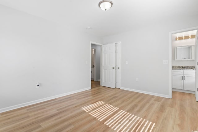 unfurnished bedroom with connected bathroom, baseboards, and light wood-style floors