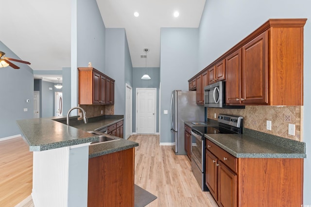 kitchen with stainless steel appliances, a sink, a towering ceiling, dark countertops, and ceiling fan