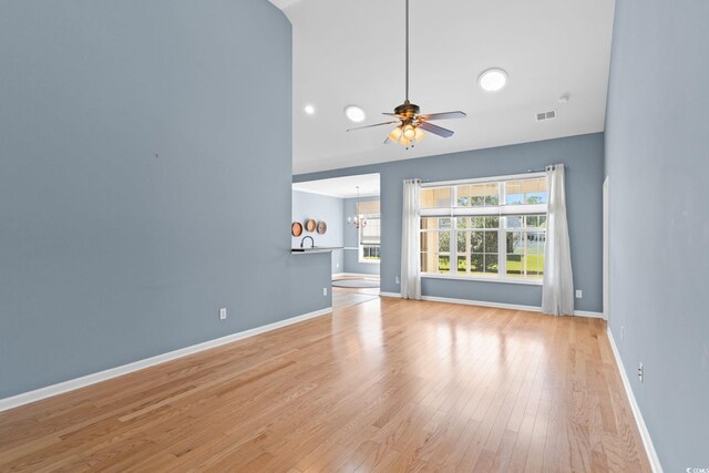 unfurnished living room featuring wood finished floors, a chandelier, baseboards, and a ceiling fan