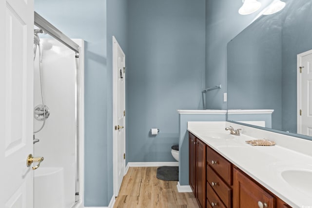 full bathroom with a stall shower, wood finished floors, double vanity, and toilet