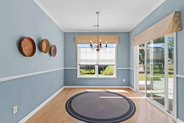 unfurnished dining area featuring wood finished floors, crown molding, baseboards, and a chandelier