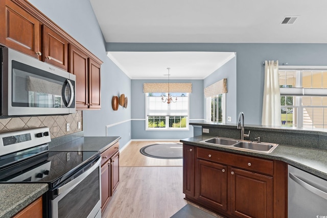 kitchen with stainless steel appliances, a sink, light wood-style flooring, dark countertops, and a chandelier