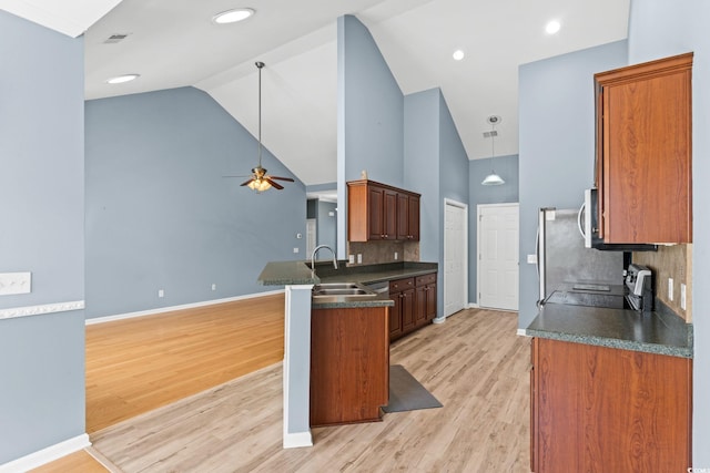 kitchen featuring dark countertops, a peninsula, appliances with stainless steel finishes, ceiling fan, and light wood finished floors