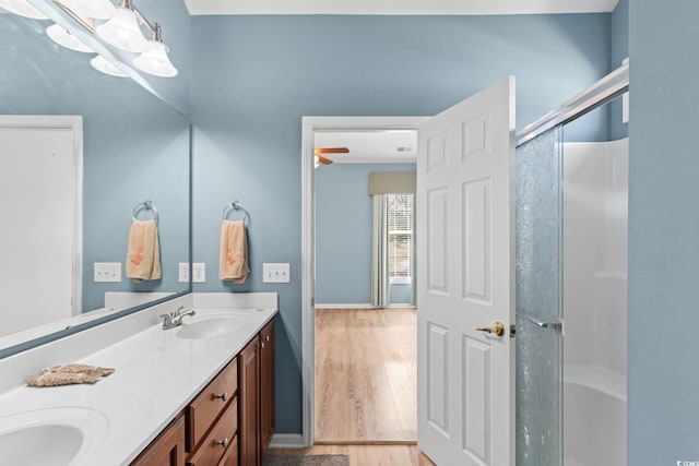 full bathroom with a chandelier, an enclosed shower, wood finished floors, double vanity, and baseboards