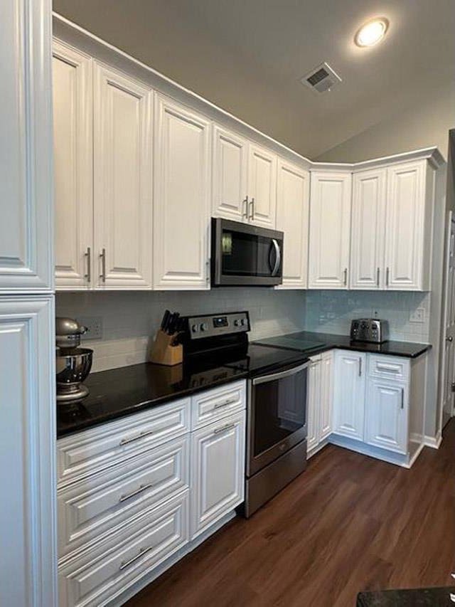 kitchen featuring dark wood finished floors, appliances with stainless steel finishes, dark countertops, white cabinetry, and visible vents