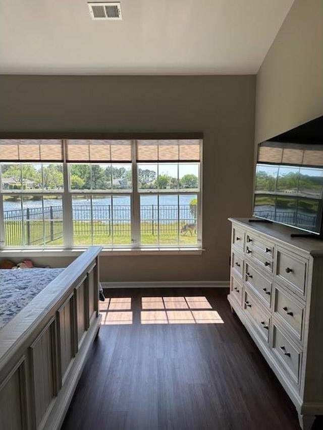 unfurnished bedroom with dark wood finished floors, visible vents, baseboards, and a water view
