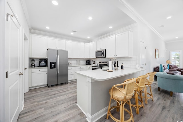 2602 Holly Dr, North Myrtle Beach, SC 29582 - kitchen featuring appliances with stainless steel finishes, a peninsula, ornamental molding, light wood-style floors, and tasteful backsplash