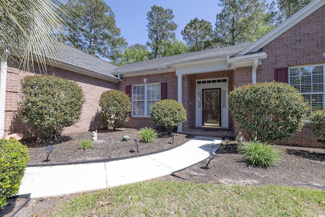 doorway to property featuring brick siding and a shingled roof