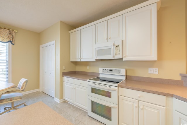 kitchen with white appliances, light tile patterned floors, light countertops, white cabinets, and baseboards