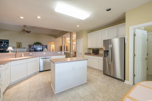 kitchen featuring white cabinets, a sink, light countertops, a kitchen island, and appliances with stainless steel finishes
