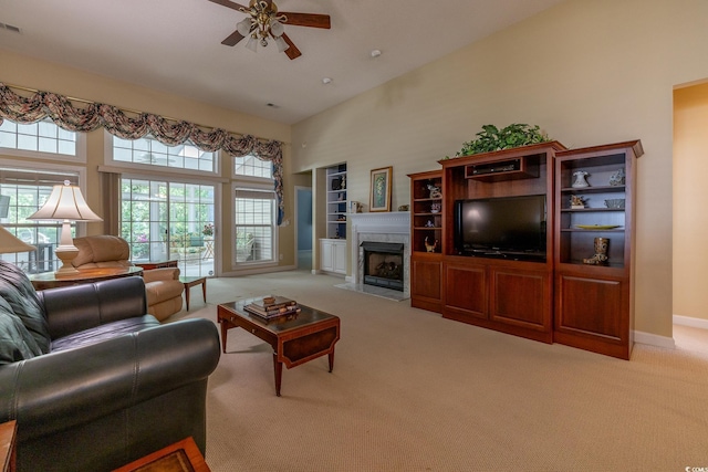 living area featuring carpet flooring, built in features, a ceiling fan, a high ceiling, and a high end fireplace