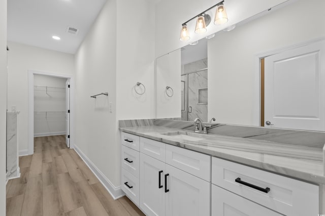 full bathroom featuring wood finished floors, a walk in closet, baseboards, a stall shower, and vanity