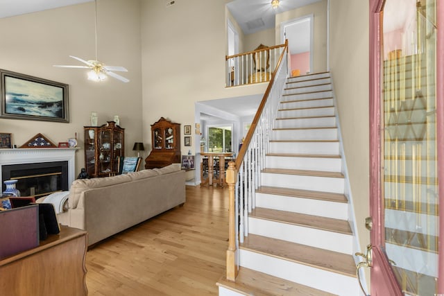 stairs with a glass covered fireplace, wood finished floors, a towering ceiling, and ceiling fan