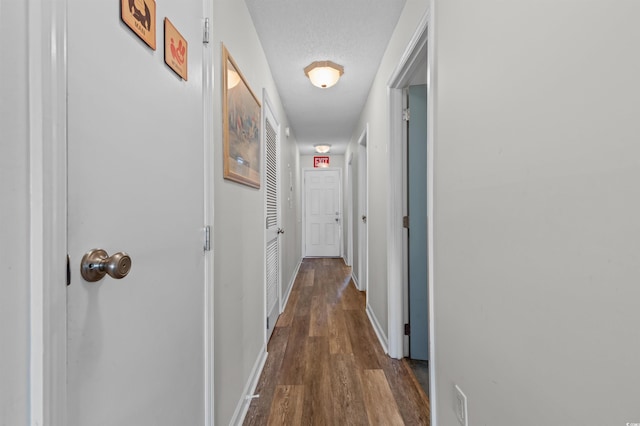 hallway with a textured ceiling, dark wood-style flooring, and baseboards
