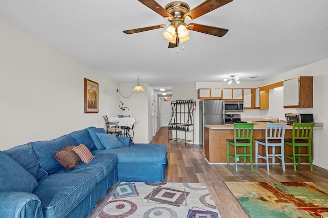 living room featuring a ceiling fan, a toaster, a textured ceiling, and wood finished floors