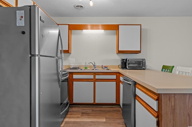 kitchen with a toaster, a sink, a peninsula, wood finished floors, and appliances with stainless steel finishes