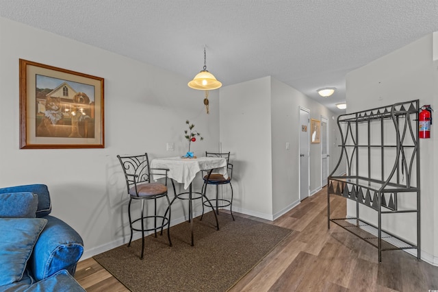 dining area featuring a textured ceiling, wood finished floors, and baseboards