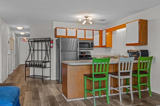 kitchen with a peninsula, a textured ceiling, dark wood-style flooring, and appliances with stainless steel finishes