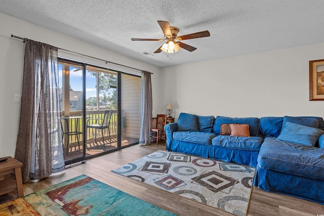 living area featuring a textured ceiling, a ceiling fan, visible vents, and wood finished floors