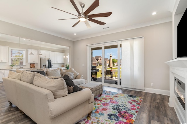 living room featuring ceiling fan, visible vents, a glass covered fireplace, ornamental molding, and dark wood-type flooring