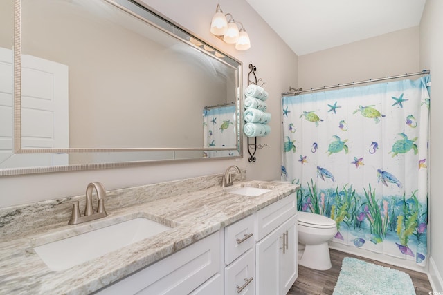 full bathroom with double vanity, a sink, wood finished floors, and toilet