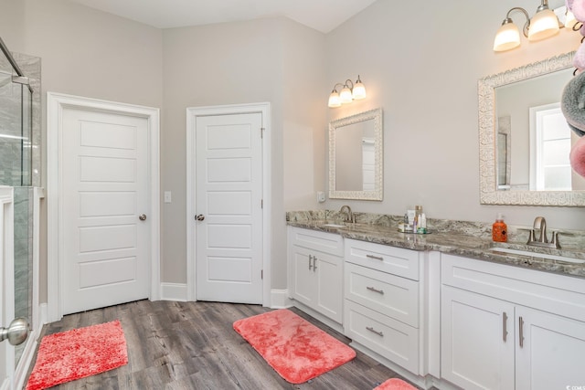 full bathroom featuring a sink, double vanity, baseboards, a shower stall, and wood finished floors