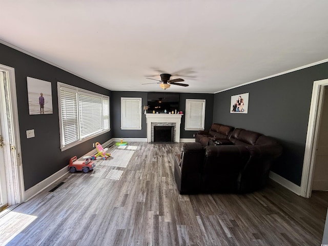 living area featuring a ceiling fan, wood finished floors, baseboards, crown molding, and a fireplace with flush hearth