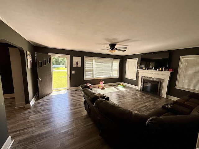 living room featuring arched walkways, a high end fireplace, dark wood finished floors, a ceiling fan, and baseboards