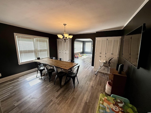 dining area featuring arched walkways, a chandelier, wood finished floors, and baseboards