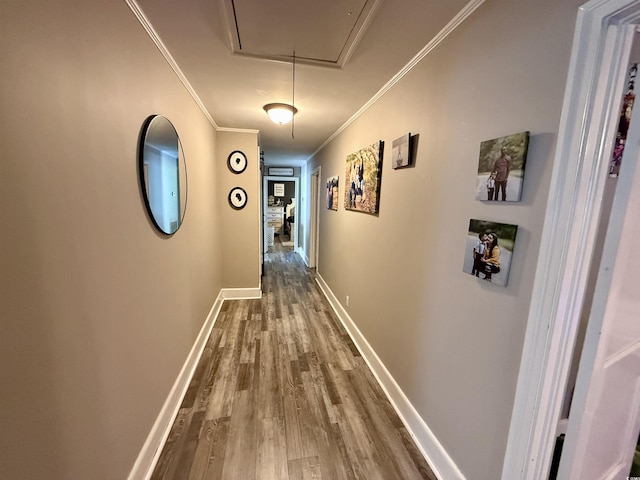 corridor with attic access, wood finished floors, ornamental molding, and baseboards