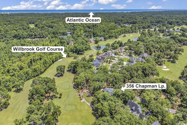 view of property location featuring a golf course, a nearby body of water, a forest, and nearby suburban area