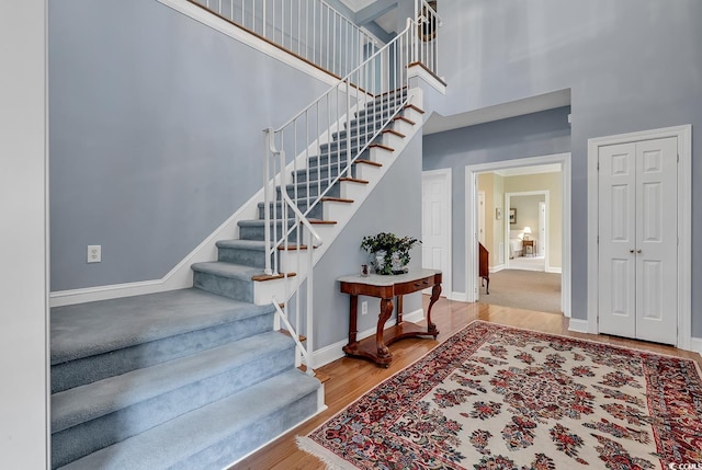 stairs featuring wood finished floors, a towering ceiling, and baseboards